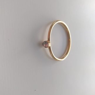 Anillo dorado fino con piedra rosa violeta sobre fondo claro