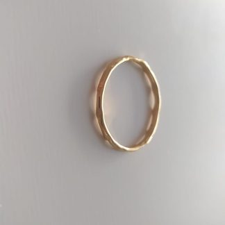 Anillo dorado fino con textura martillada irregular sobre fondo claro