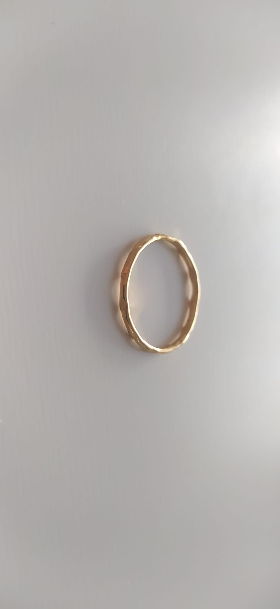 Anillo dorado fino con textura martillada irregular sobre fondo claro