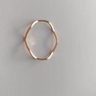 Anillo dorado de forma ondulada sobre superficie clara