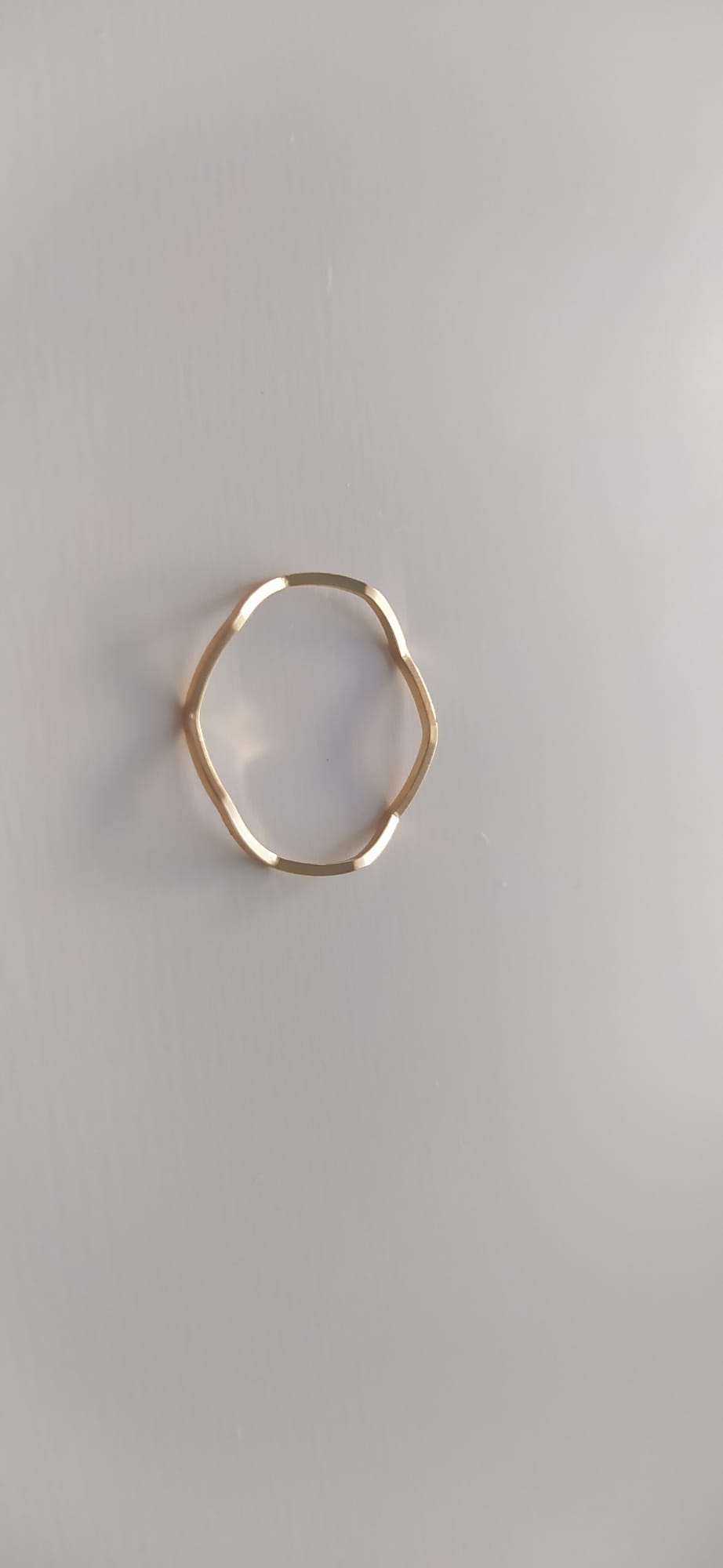 Anillo dorado de forma ondulada sobre superficie clara