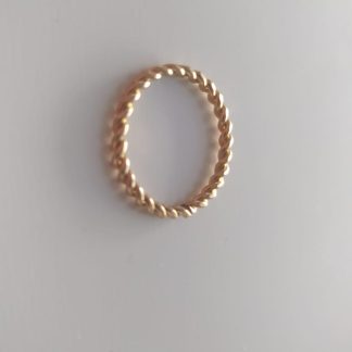 Anillo dorado con textura trenzada sobre fondo claro