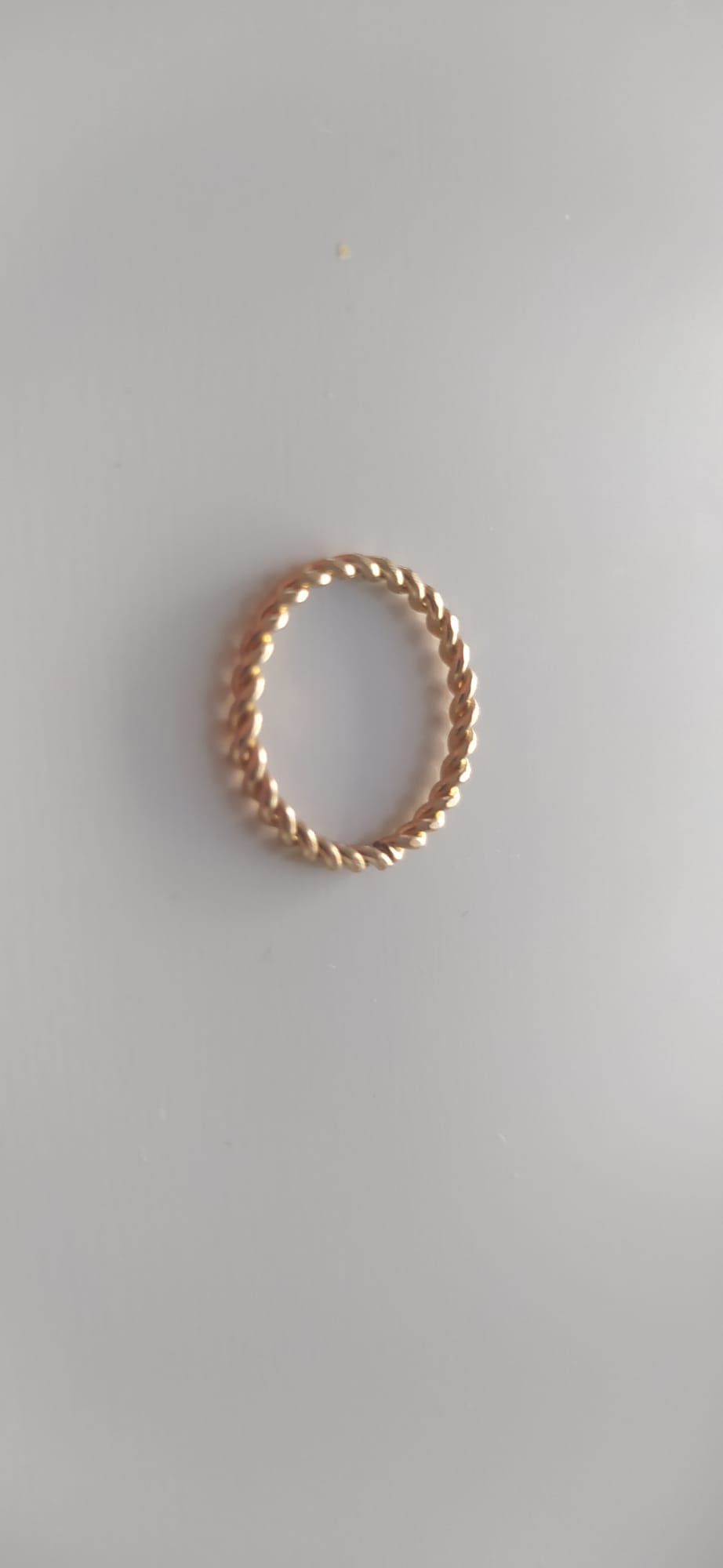Anillo dorado con textura trenzada sobre fondo claro