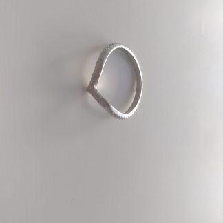 Anillo plateado con forma en V y textura granulada sobre fondo claro