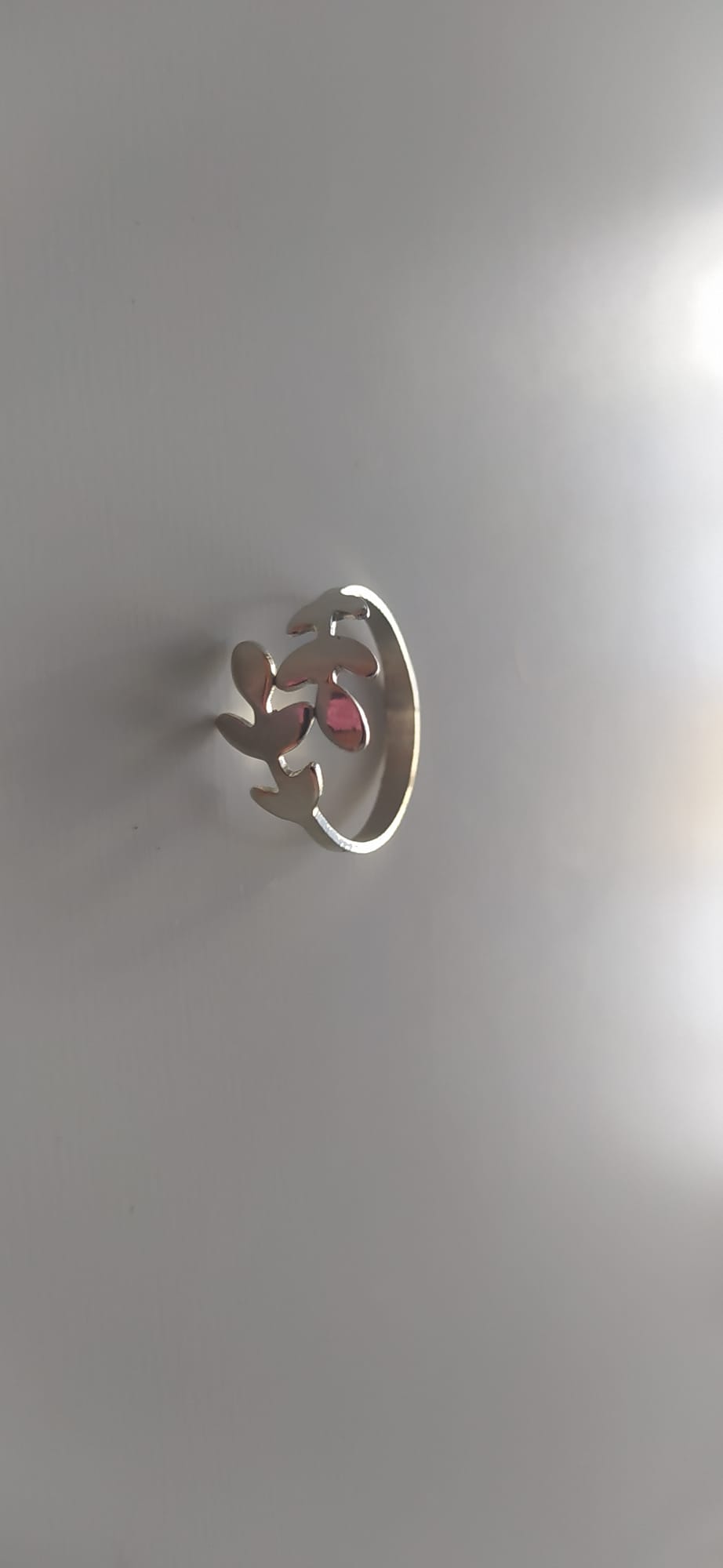 Anillo plateado con diseño calado de hojas y ramita sobre fondo claro