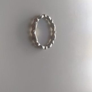 Anillo plateado de líneas onduladas y textura irregular sobre fondo claro
