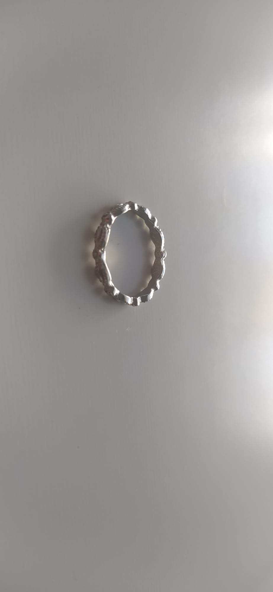 Anillo plateado de líneas onduladas y textura irregular sobre fondo claro