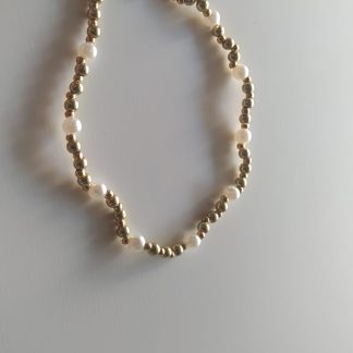 Pulsera elástica de bolitas doradas y perlas naturales sobre fondo claro