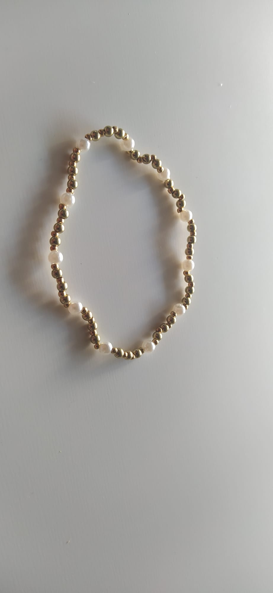 Pulsera elástica de bolitas doradas y perlas naturales sobre fondo claro