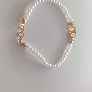 Pulsera de perlas blancas con cierre dorado en forma de corazones sobre fondo claro